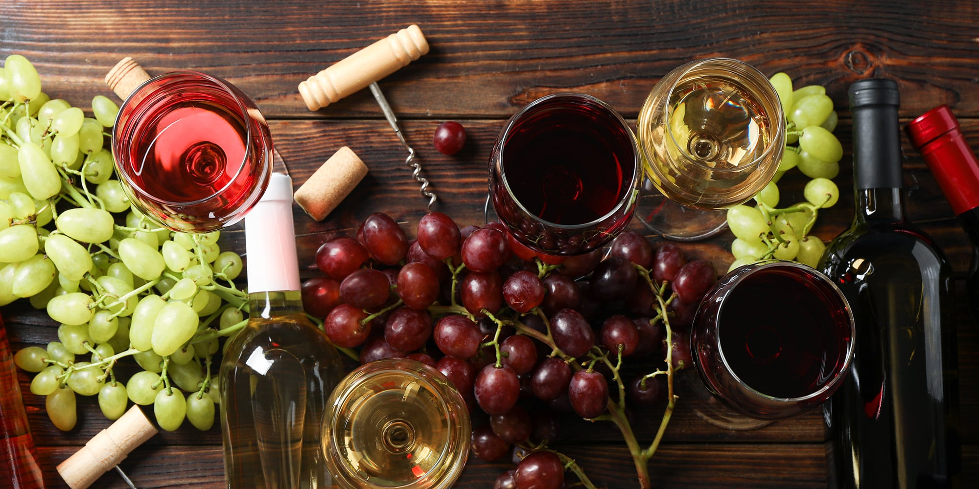 Flat lay. Grapes, corkscrew, bottles and glasses with wine on wo